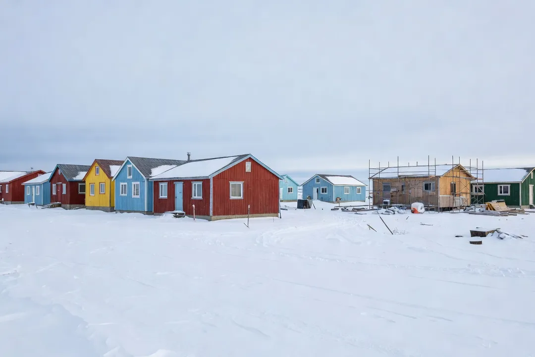 Rangée de maisons nordiques colorées à Kuujjuaq en hiver, avec chantier de construction en arrière-plan